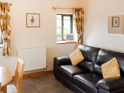 a living room with a black leather couch at Red Kite Cottage in Llangunllo