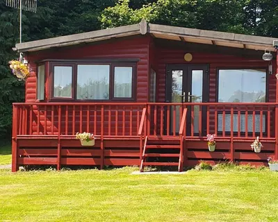a red cabin with a large deck in the grass at Number 8 Lodge Caer Beris in Maesmynis