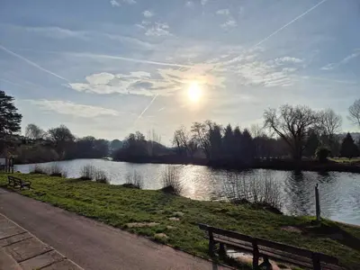 a bench next to a river with the sun in the sky at Number 8 Lodge Caer Beris in Maesmynis