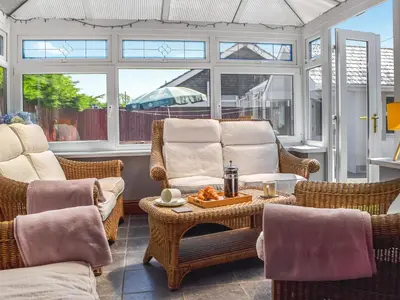 a conservatory with wicker chairs and a table and windows at Ferwig in New Quay