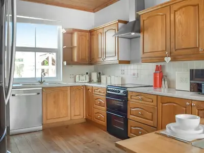 a kitchen with wooden cabinets and a black dishwasher at Ferwig in New Quay