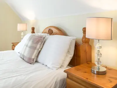 a bed with white pillows and a table with a lamp at Ferwig in New Quay
