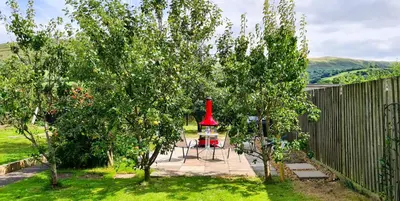 a garden with an apple tree and a red bell tower at Awelfa a peaceful cottage in the Cambrian mountains in Llanbrynmair