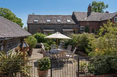 a patio with a table and umbrella in front of a house at Gooseyard at Middle Farm and Cottages in Picklescott