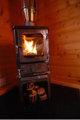 a wood stove with a fire in a room at LARCHES LODGE Norwegian log cabin, wood stove & spa in Church Stretton