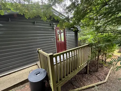 a house with a wooden porch with a red door at LARCHES LODGE Norwegian log cabin, wood stove & spa in Church Stretton