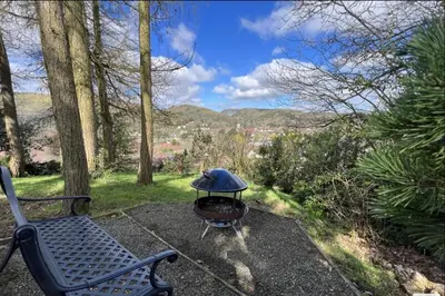a grill sitting next to a bench in a yard at LARCHES LODGE Norwegian log cabin, wood stove & spa in Church Stretton