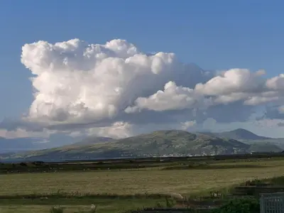 a field with a mountain in the background with clouds at Snowdonia Holiday Sea Beach and Mountains view in Llwyngwril