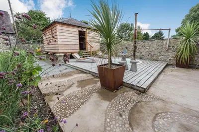 a small wooden deck with a house and a palm tree at Ty Glyn Mansion Cottage in Ciliau-Aeron