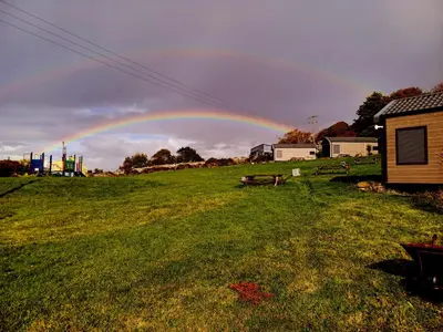 a rainbow in the sky over a field at Cabin Cynthia in Llwyngwril
