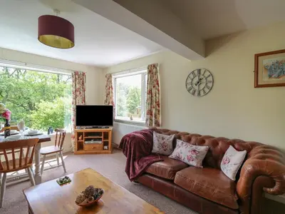 a living room with a brown leather couch and a table at Nuthatch Cottage at Riverside Lodge in Rhayader