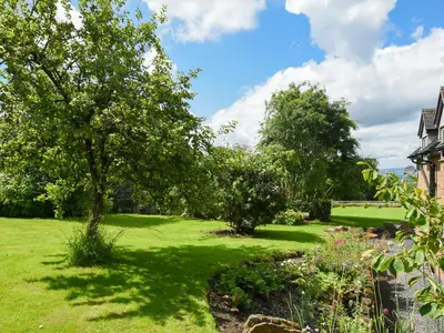 a garden with trees and flowers in front of a house at The Lodge At Harvest Farm in Ludlow