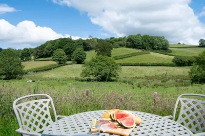 a table with a plate of watermelon on top of a field at Birch Banc Retreats - Glyn-Haul, New Enc Decking in Llanidloes