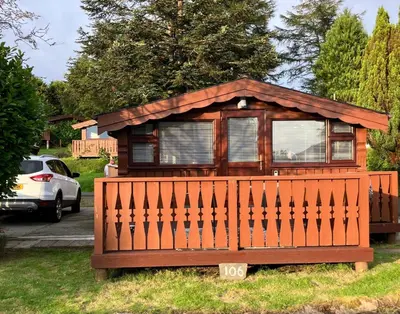 a small house with a fence in the grass at Snowdonia luxury log cabin in Trawsfynydd