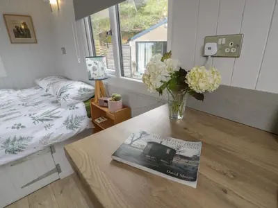 a room with a bed and a table with a vase of flowers at Shepherd's Hut at Penrallt Goch in Blaenau-Ffestiniog