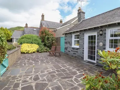 a patio with two chairs in front of a house at Ty Llaeth Cottage in Tywyn
