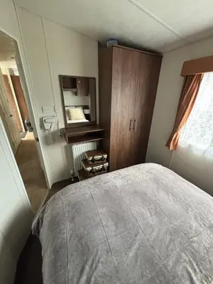 a bedroom with a bed and a cabinet and a window at Modern 2017 model Delta Sienna static caravan in Clarach Bay in Aberystwyth