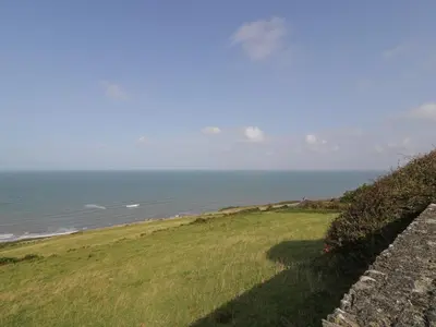 a grassy hill with the ocean in the background at Tarrenhendre Pod in Tywyn
