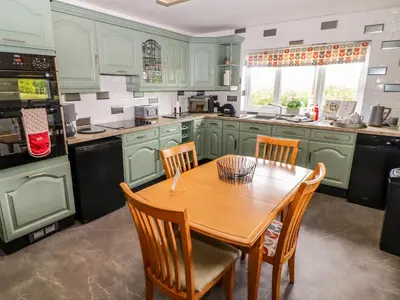 a kitchen with green cabinets and a wooden table and chairs at Morva in New Quay
