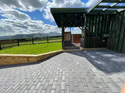 a patio with a green building and a grassy field at Little Cottage of the Beacons in Brecon
