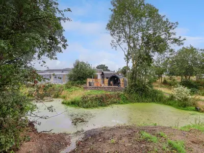 a body of water with a house in the background at Heron Pod in Oswestry
