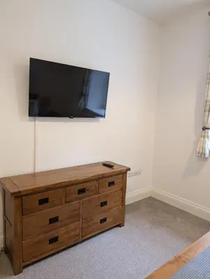 a flat screen tv on a wall with a wooden dresser at 2 Chapel Nazareth in Penrhyndeudreath
