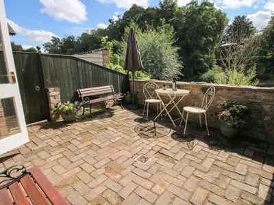 a patio with a table and an umbrella and a bench at Moorhen Cottage in Ludlow