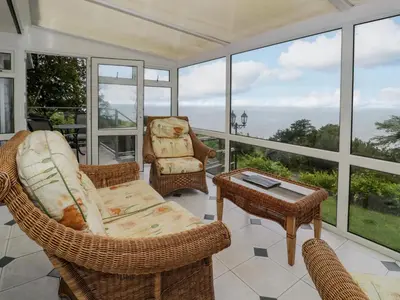 a screened in porch with wicker furniture and windows at Woodland Roost in Barmouth