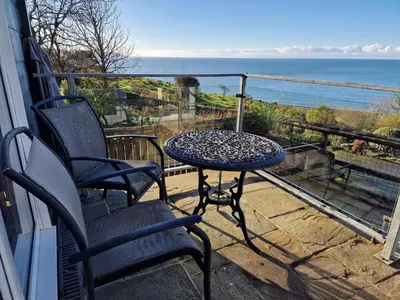 a table and chairs on a balcony with the ocean at Woodland Roost in Barmouth