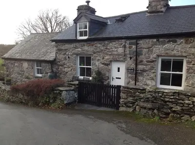 an old stone house with a black fence at Garth Engan B&B with private lounge in Llanbedr