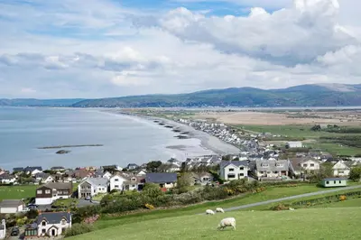 a town with sheep grazing on a hill next to the ocean at Morwylfa Borth and Ynyslas in Borth