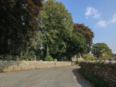 a stone wall next to a road with trees at New Inn Cottage in Church Stretton