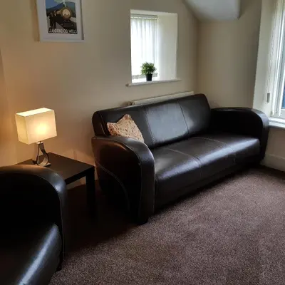 a black leather couch in a living room with a lamp at Ty Morgan's Apartments in Rhayader