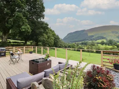a wooden deck with a couch and a table and chairs at Caban Tirion in Machynlleth