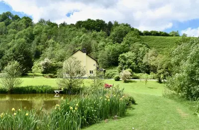 a house in the middle of a garden with a pond at Secluded Farmhouse with Private Lake in Llanwrda
