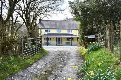 a yellow house with a fence and a dirt road at Secluded Farmhouse with Private Lake in Llanwrda