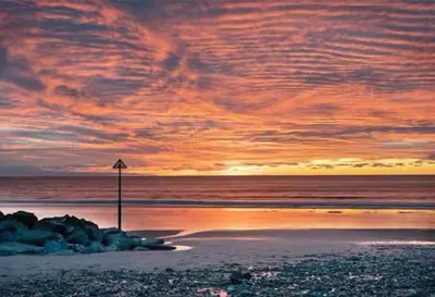 a sunset on a beach with a pole in the sand at Y Mor Cosy Apartment in Tywyn