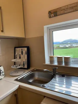 a kitchen with a sink and a window with cups at Y Mor Cosy Apartment in Tywyn