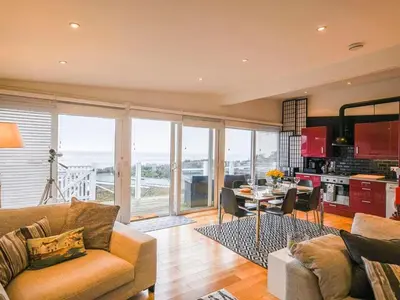 a living room with a couch and a table and a kitchen at The Glass House in Aberdyfi