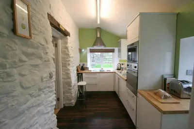 a kitchen with white cabinets and a stone wall at Hen Ffermdy Aberaeron in Cross Inn