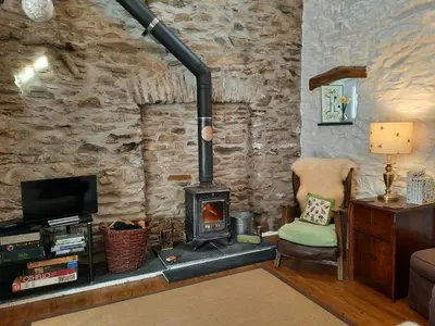 a living room with a wood stove and a chair at Hen Ffermdy Aberaeron in Cross Inn