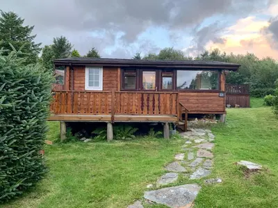 a wooden house with a large deck in a yard at Caban Marjie in Trawsfynydd