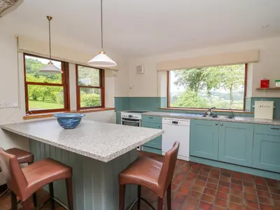 a kitchen with blue cabinets and a counter with stools at Oak Apple Cottage in Presteigne