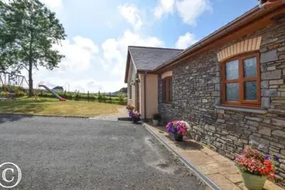 a stone house with a playground in the background at Aberystwyth Dinas Cottage in Llanilar