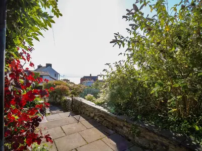 a garden with red flowers and a stone pathway at 1 Gibraltar Terrace in Aberdyfi
