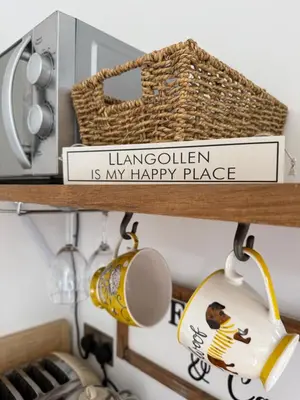 a kitchen shelf with a happy place sign and a basket at Castle View chalet in Llangollen