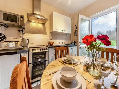 a kitchen with a wooden table with red flowers on it at Snowdrop in Llanerch-Aeron