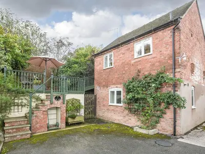 a brick house with a staircase and an umbrella at The Corn House - Cottage in Great Hanwood