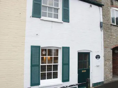 a white building with green shutters and a door at Troutbeck Cottage in Ludlow