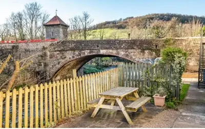 a wooden picnic table in front of a stone bridge at Glanyrafon Cottage in Sennybridge